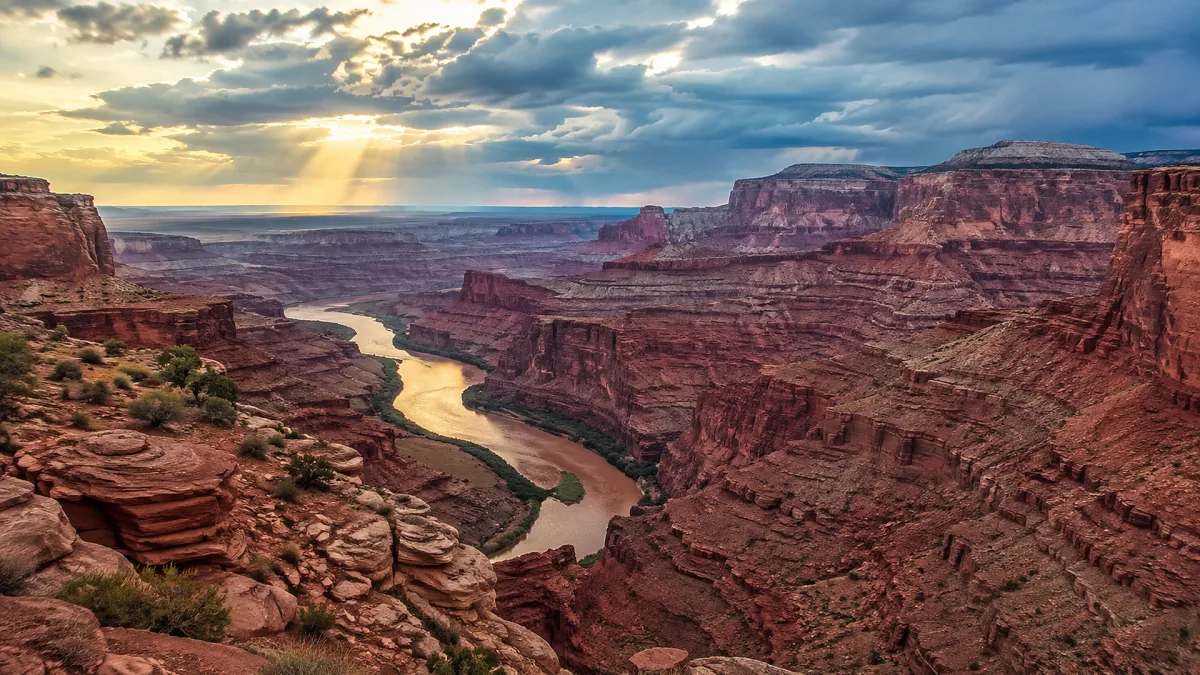 A river cuts through a red canyon beneath heavy storm clouds.