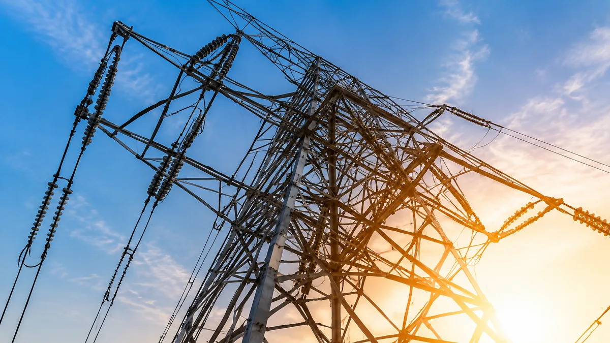 A high-voltage transmission tower rises into bright sun with power lines stretching across the sky.