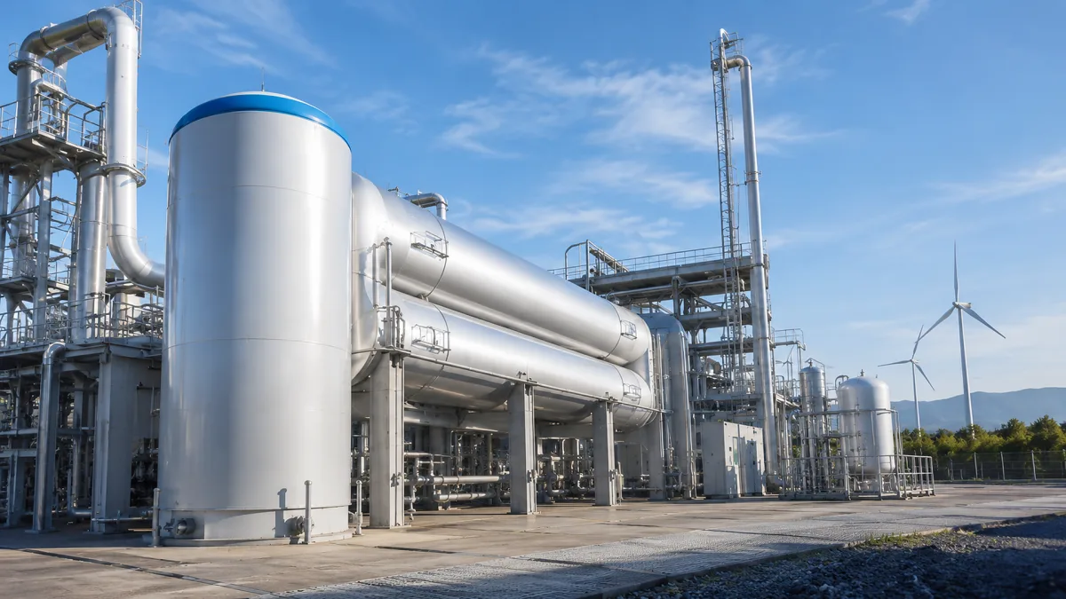 White hydrogen storage tanks and pipes stand near a wind turbine in a clean energy facility.