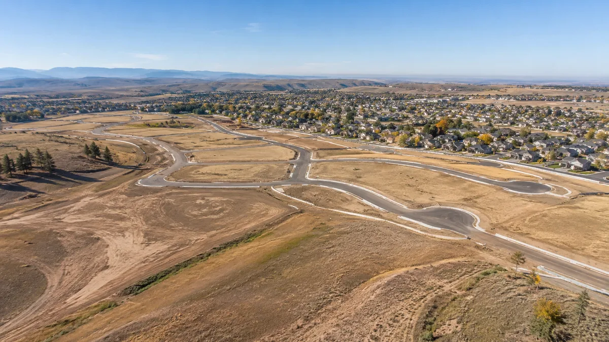 An aerial view shows graded land, new roads, lots, and early infrastructure for a large residential subdivision development.