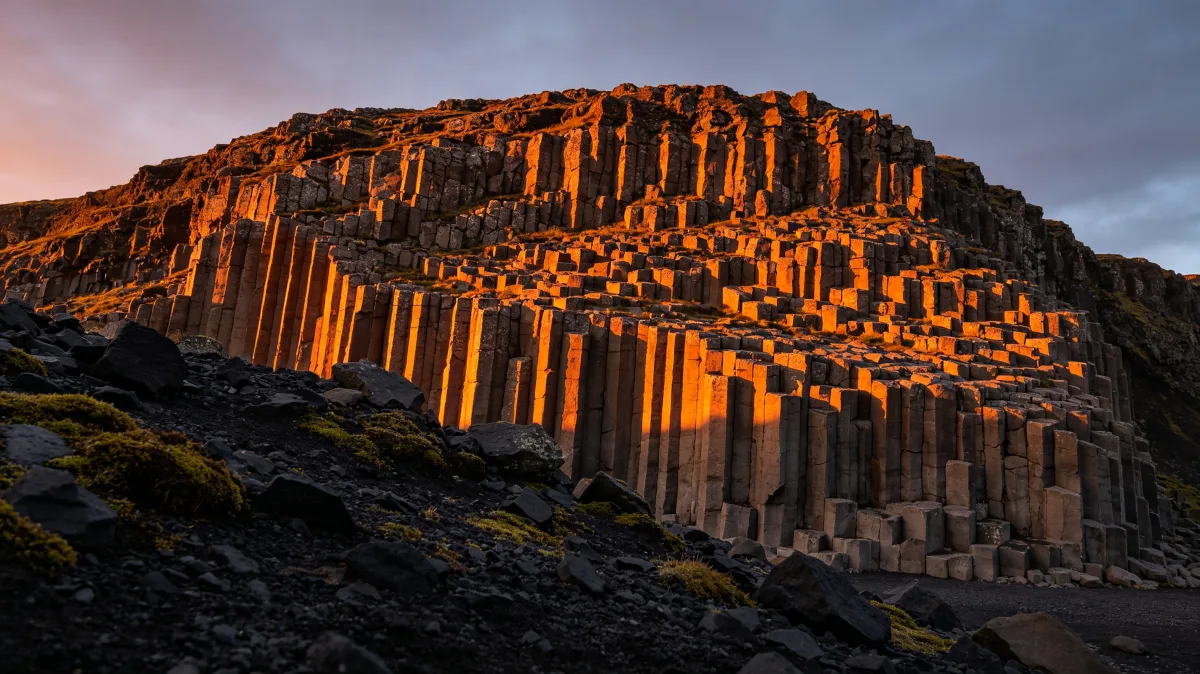vertical basalt columns form a dramatic mountain wall at orange dusk.