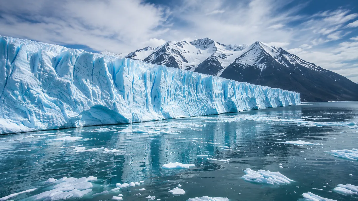 A glacier face reflects in cold blue water with floating ice.