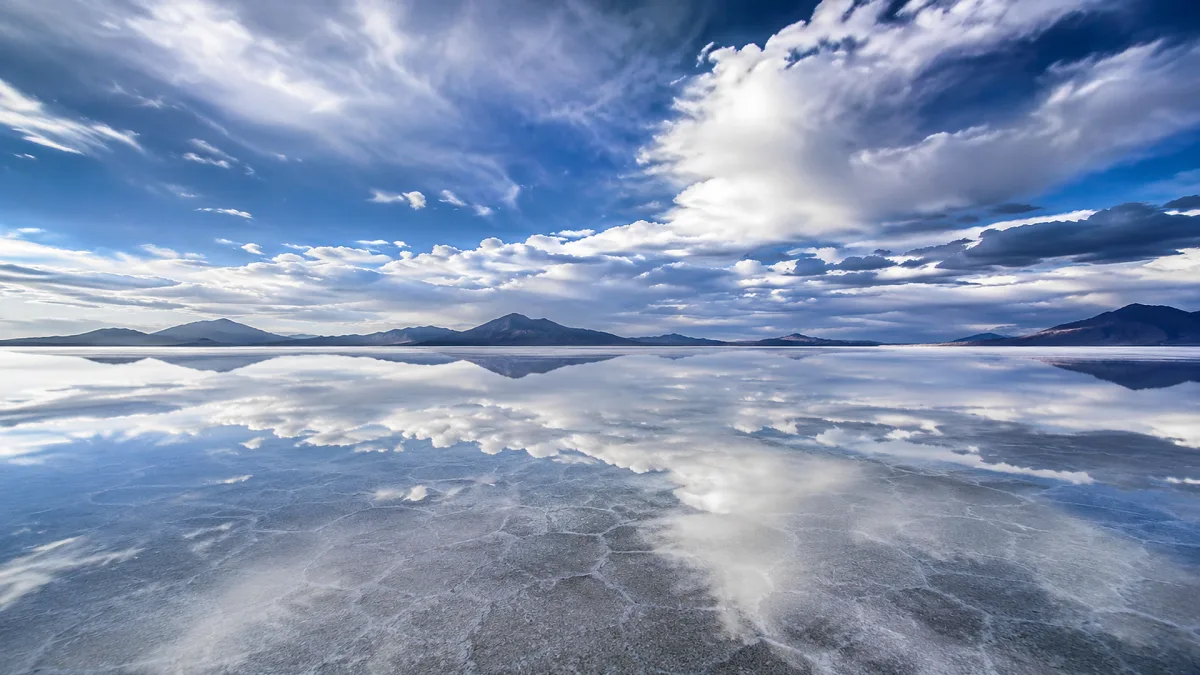 A mirror-like salt flat reflects dramatic clouds and distant mountains.