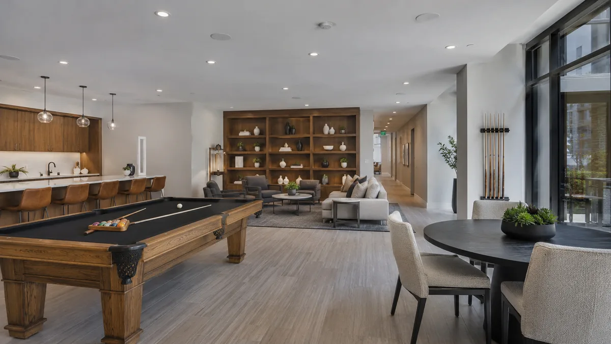 An open-plan luxury recreation room includes a pool table, bar, lounge seating, large windows, and polished wood flooring.