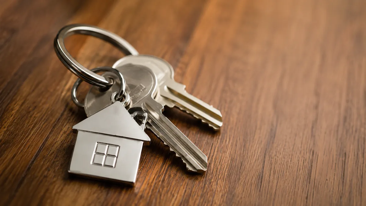 A set of house keys with a small house keychain rests on a wooden table as a simple home ownership concept.