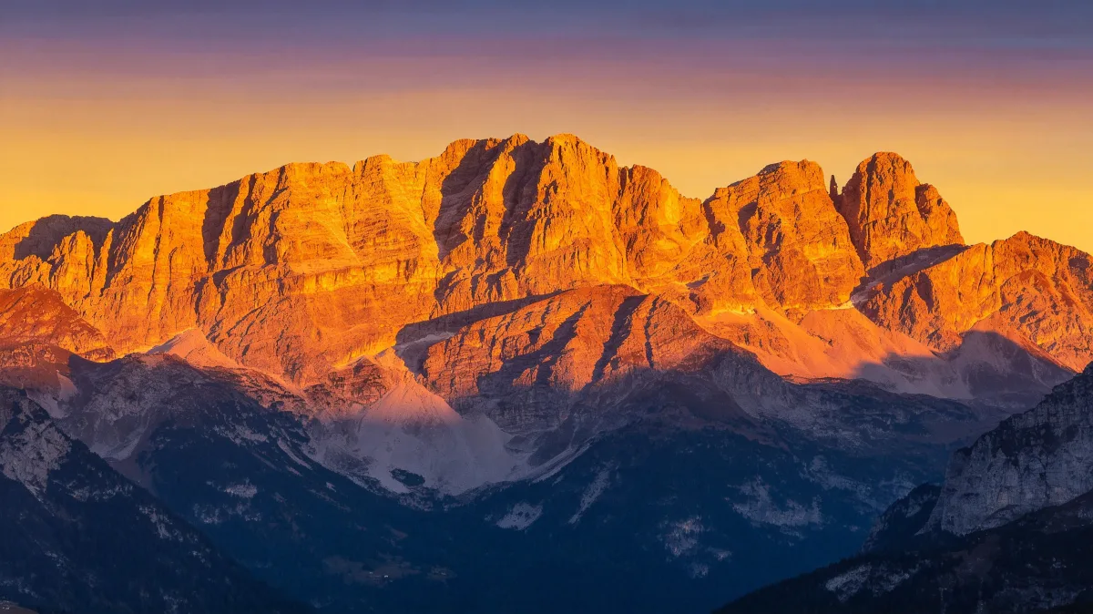 golden alpenglow illuminates a long ridge of high mountain peaks.