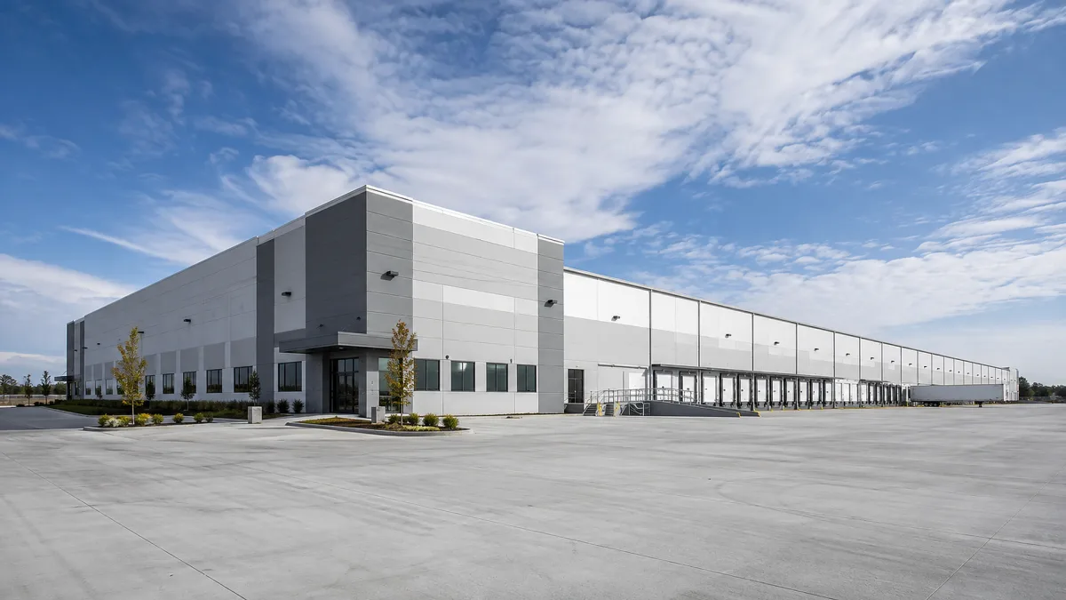 A large industrial warehouse property has loading doors, white facade, broad paved apron, and an expansive logistics-ready footprint.
