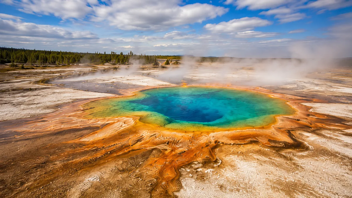 A bright geothermal hot spring glows turquoise among orange mineral terraces and steam.