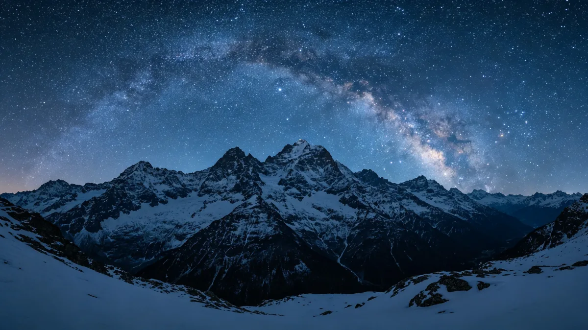 the milky way arcs above snow-covered mountains in a cold night panorama.