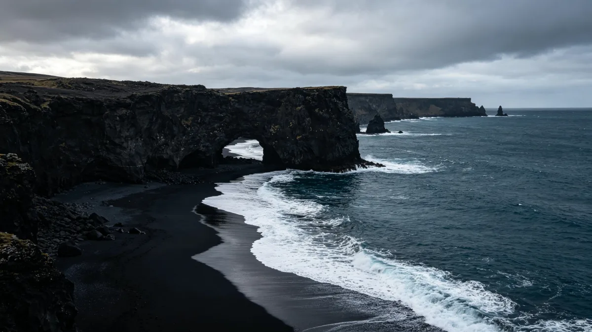 black sand beach and tall sea cliffs meet a stormy gray coastline.