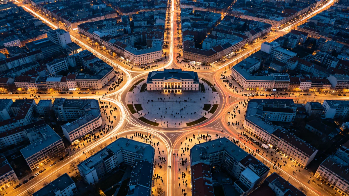 an aerial city traffic circle glows around a central civic building at night.