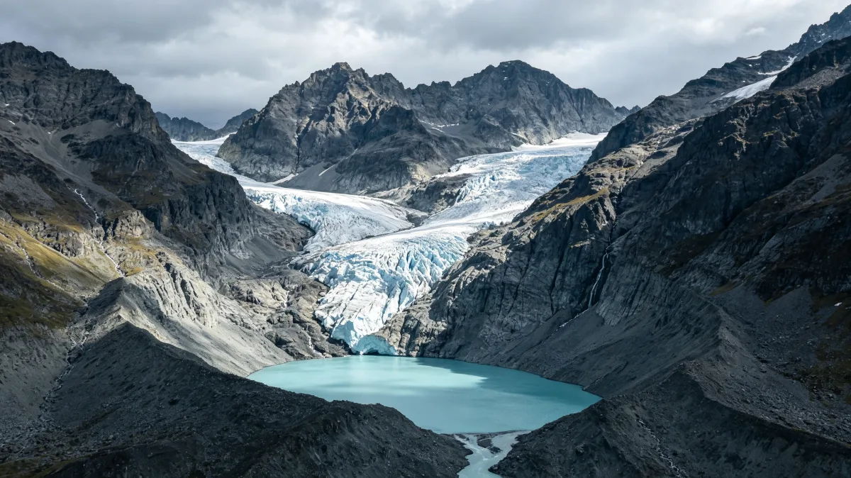 a broad glacier field spreads across high alpine mountains under streaked clouds.