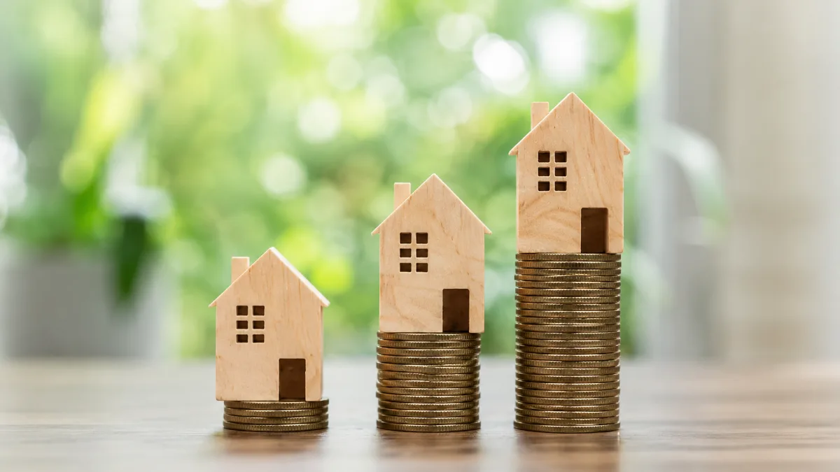 Wooden house models stand on rising stacks of coins, suggesting property value growth, investment, and housing finance.