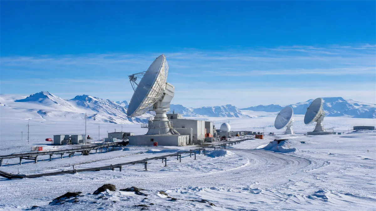 White satellite dishes operate across a frozen polar station under a crisp blue sky, representing remote connectivity, scientific communication, satellite internet, and reliable signal links in...