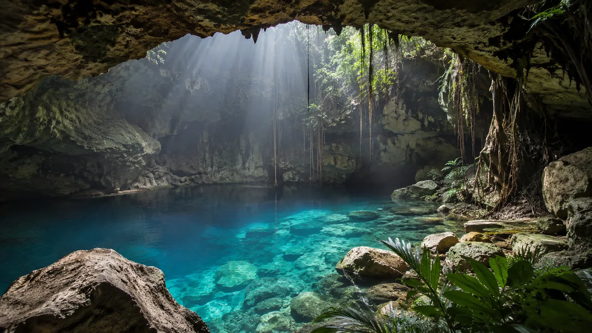 A blue cave lagoon glows with clear water beneath a rocky natural opening.