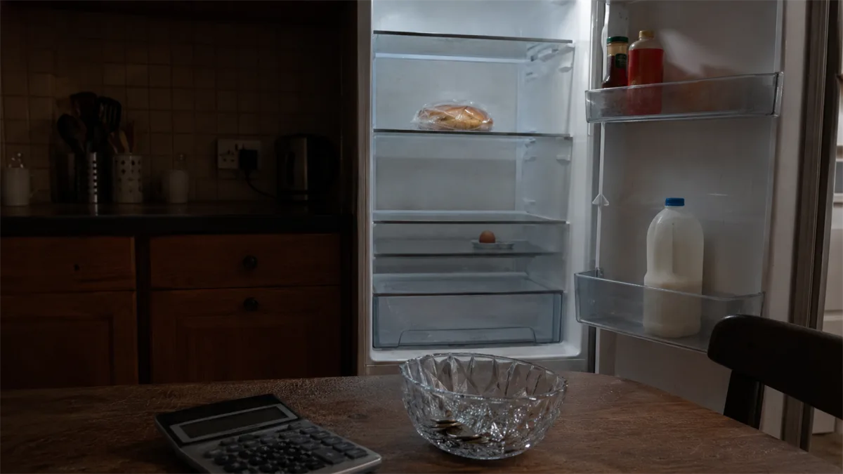 A nearly empty refrigerator, calculator, and bowl show food insecurity, low pantry reserves, and the practical side of household budgeting.