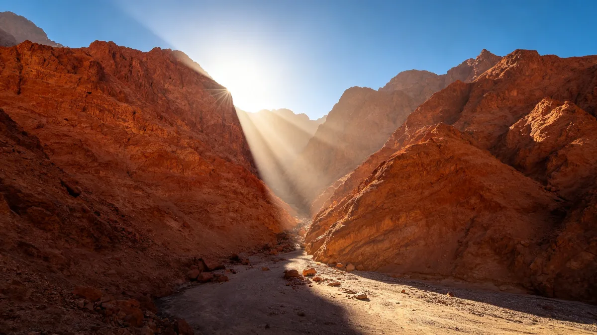a shaft of sunlight pours into a narrow red mountain canyon pass.